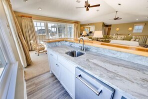 A modern kitchen with a marble countertop, a built-in sink, and a ceiling fan. - The Lawrence at Ships Watch in Duck Fabulous Ocean Front Home (Duck)