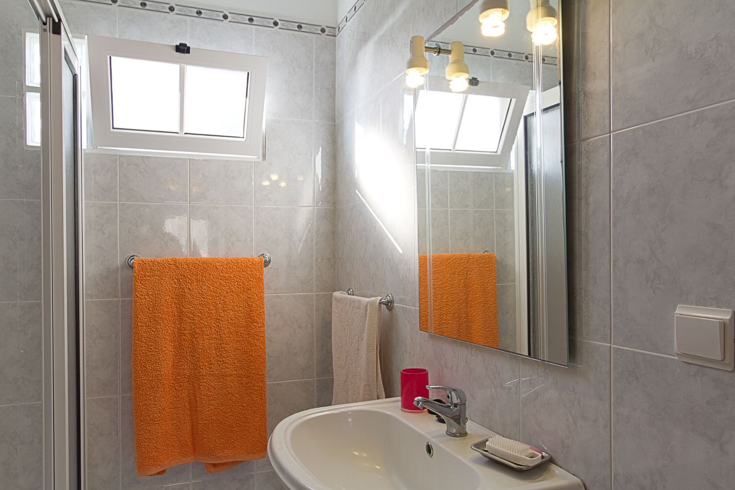 A bathroom with a glass shower enclosure, a sink with a mirror, and two towels, one orange and one beige.