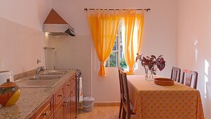 A kitchen with a sink, stove, and cabinets. There is a window with yellow curtains and a view of greenery outside.