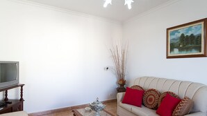 A living room with a sofa, a coffee table, a television on a stand, and a painting on the wall.