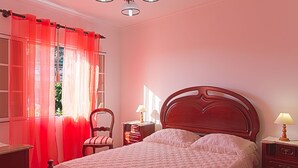 A bedroom with a bed, a chair, a nightstand, and a lamp.
