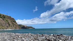 A rocky beach with a clear sky and distant hills.