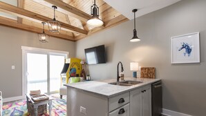 Une cuisine dotée d’un îlot central intégré, de poutres en bois au plafond, d’un téléviseur à écran plat et d’un tapis aux couleurs vives.