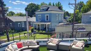 Une terrasse extérieure aménagée avec des meubles en osier et un gazon synthétique, le tout entouré d’une rambarde en métal.