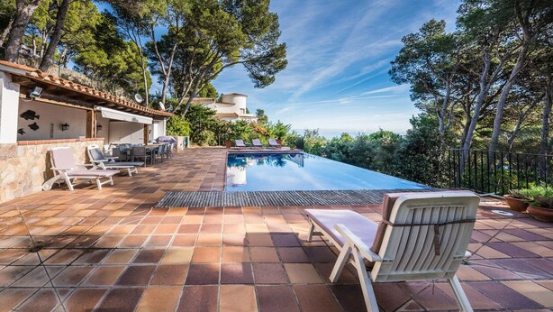 A swimming pool with lounge chairs and a pergola, surrounded by trees and a stone wall. - You cook, eat and relax around the pool with nice sea view. (Palafrugell)
