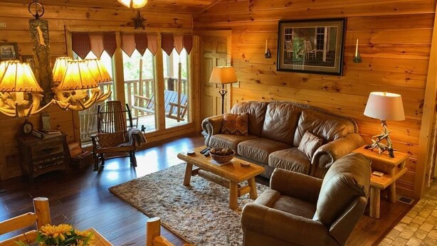 L’intérieur chaleureux d’un chalet avec un plafond en bois, un canapé en cuir, une table basse en bois et une lampe rustique.