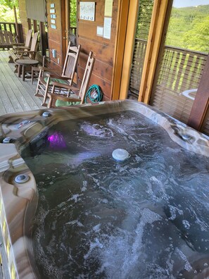 A hot tub with a wooden deck, chairs, and a view of the landscape.