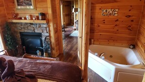 Une chambre confortable dans un chalet en bois, avec une cheminée, un grand lit, une baignoire et un couloir menant à une autre pièce.