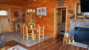 L’intérieur d’un chalet en bois comprend une table à manger, des chaises, une cheminée et un téléviseur.