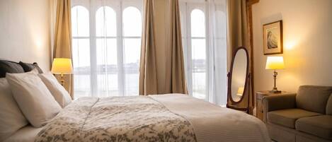 A hotel room with a large bed, two bedside lamps, a mirror, a sofa, and a window with curtains.