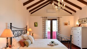 Een slaapkamer met een bed, bedlampen, een dressoir, een kroonluchter en een raam met gordijnen.