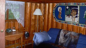 En mysig stuga med träpanel i taket, en blå soffa, ett litet bord med en lampa och en väggmålning.