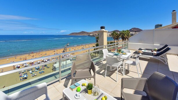 Un balcon avec vue sur la plage, des sièges d’extérieur et une table avec des livres et des citrons.