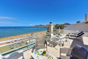 Varanda com vista para a praia, mobiliário de exterior e uma mesa com livros e limões.