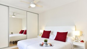 Une chambre d’hôtel avec un grand lit, deux oreillers rouges, une table de chevet avec une lampe et un plateau contenant des articles pour le petit-déjeuner.