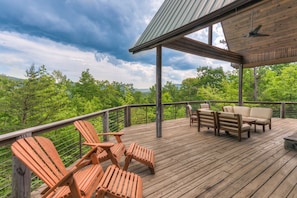 A wooden deck with Adirondack chairs and a sofa, overlooking a forested area. - Serene Mountain Views: Pet-Friendly Retreat with Hot Tub (Mill Spring)