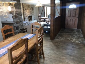 A dining area with a stone fireplace, wooden furniture, and a view of a living room with a sofa and a TV. - HaT Ranch Lodge. Perfect for a large group or multiple families. NO CLEANING FEE (Ponca City)