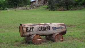 A wooden sign with the text "HAT RANCH" and an arrow pointing to the right, placed on a grassy field with a stone building in the background. - HaT Ranch Lodge. Perfect for a large group or multiple families. NO CLEANING FEE (Ponca City)