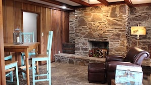 A rustic interior with a stone fireplace, wooden furniture, and a leather armchair. - HaT Ranch Lodge. Perfect for a large group or multiple families. NO CLEANING FEE (Ponca City)