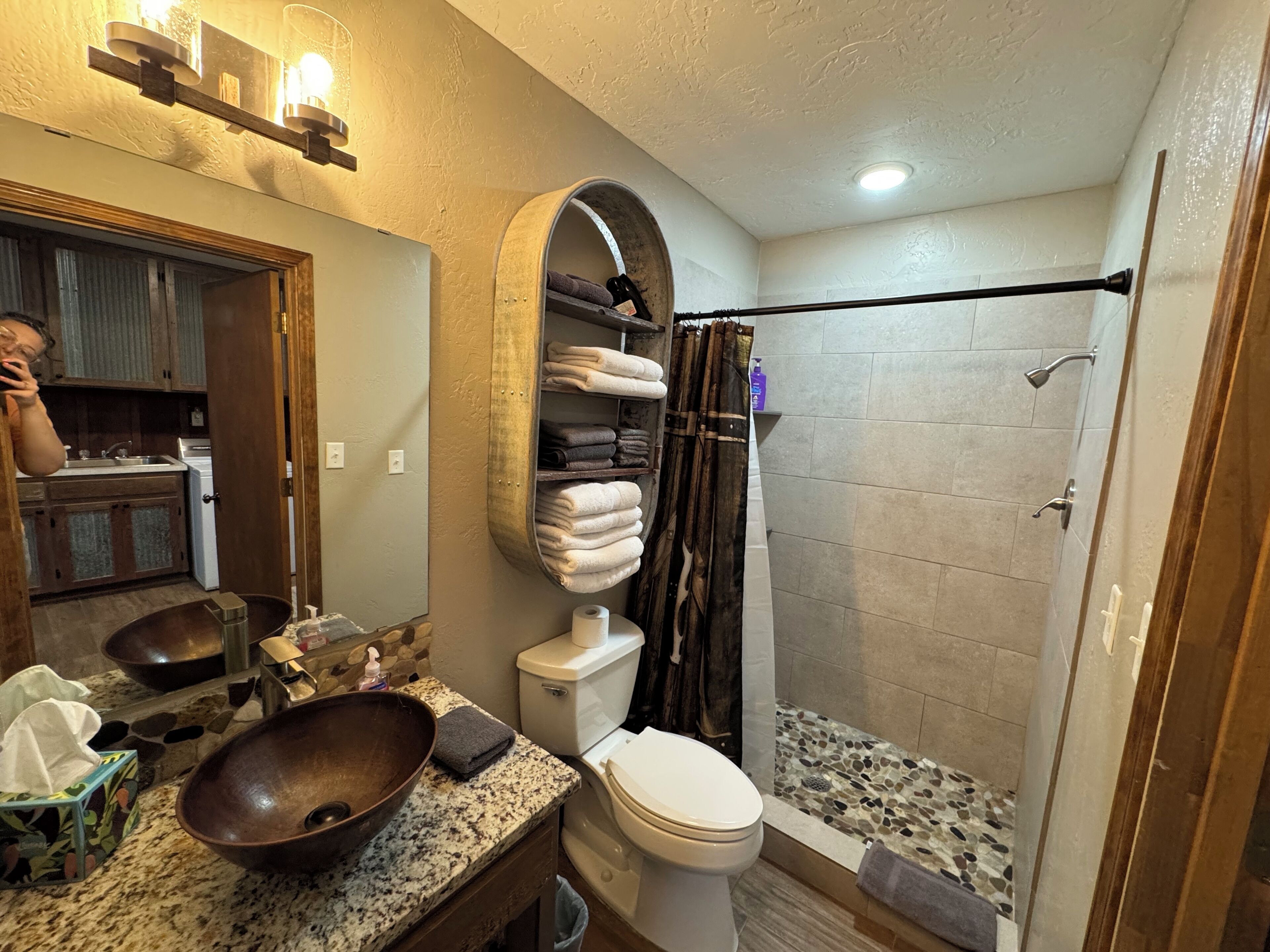 Un bagno con un ampio specchio, un lavabo in legno, un water e una doccia rivestita di mosaici.