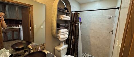 Un bagno con un ampio specchio, un lavabo in legno, un water e una doccia rivestita di mosaici.