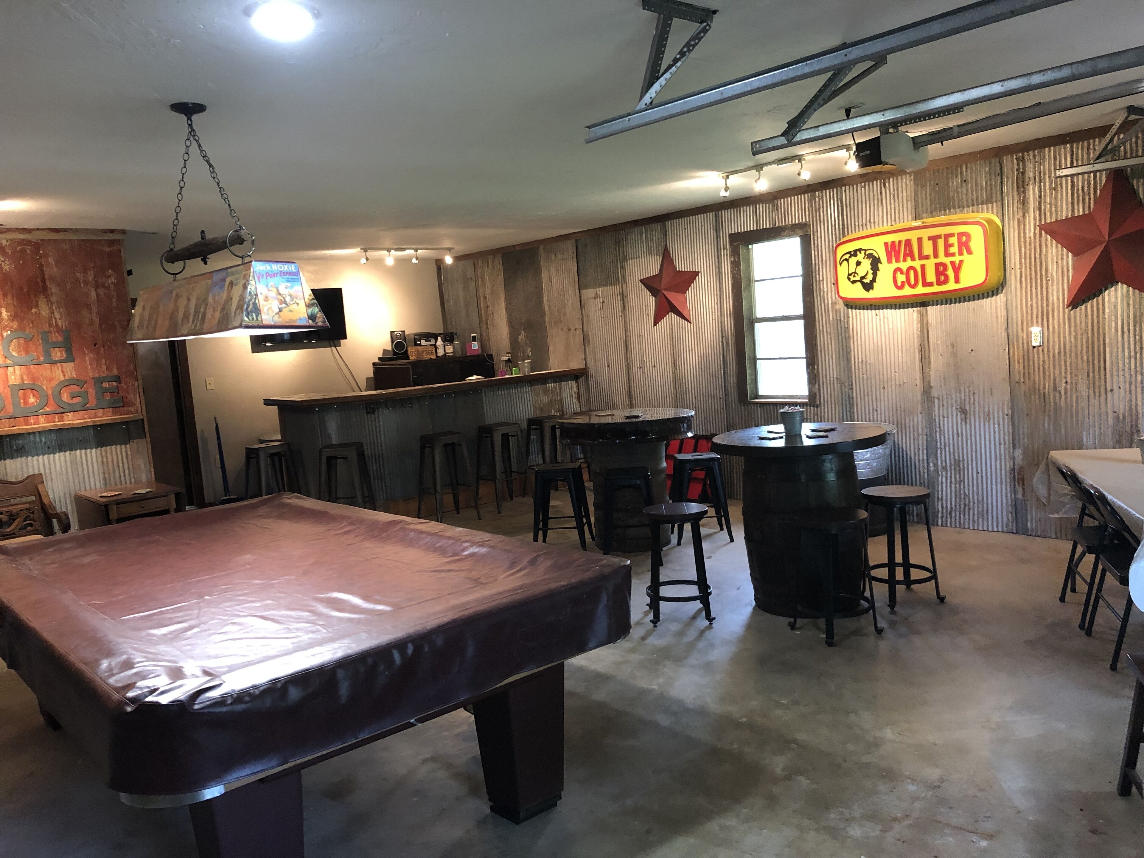 A billiards table in a room with a bar area, stools, and a sign reading "WALTER COLBY".