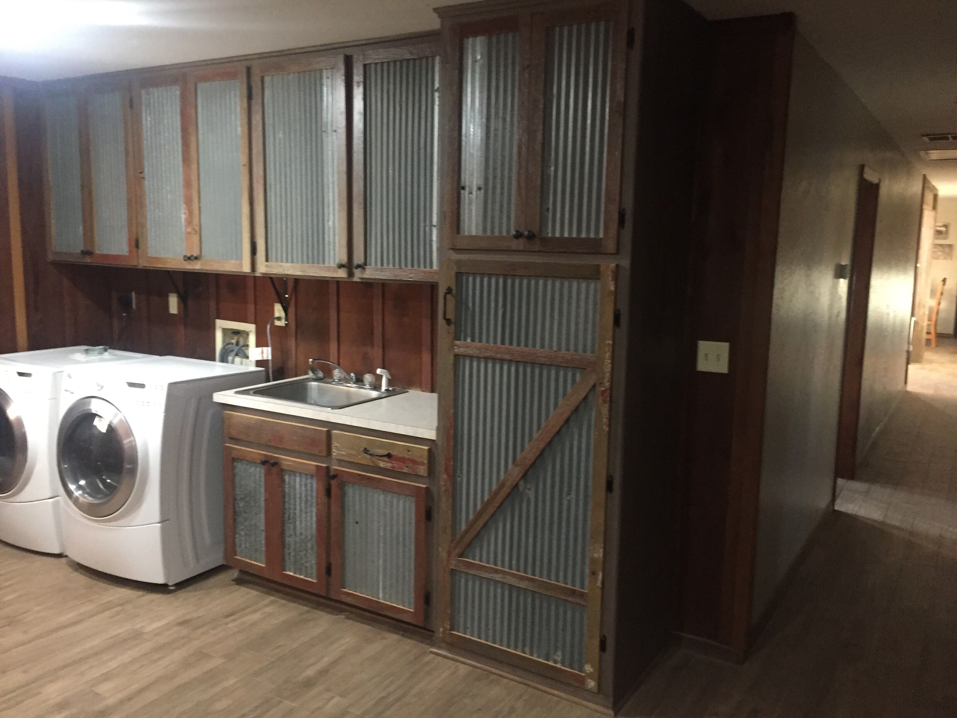 A laundry room with a washing machine, a sink, and wooden cabinets.