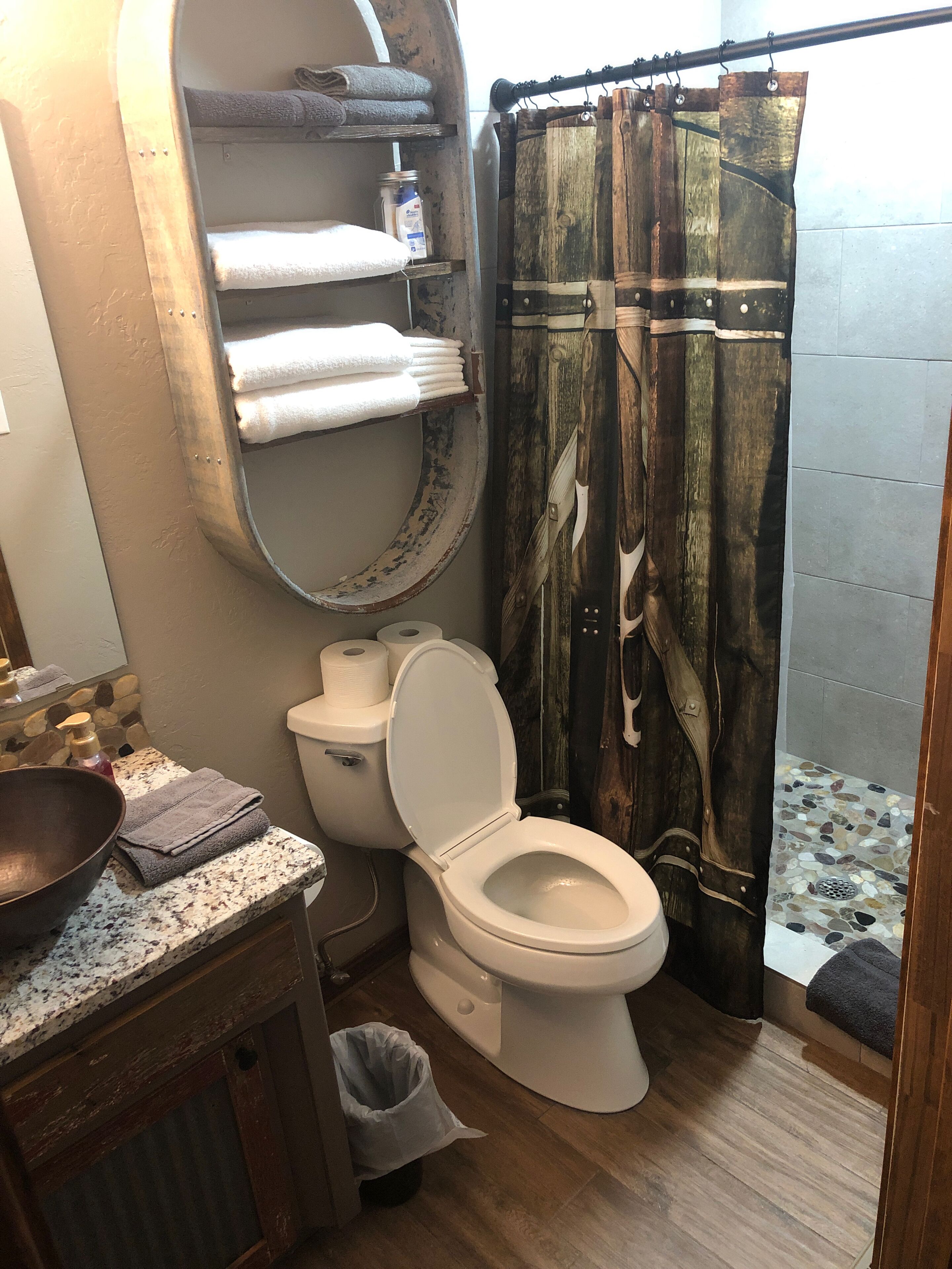 A bathroom with a rustic design, including a wooden toilet, a large mirror, and a shower curtain with a distressed wood pattern.