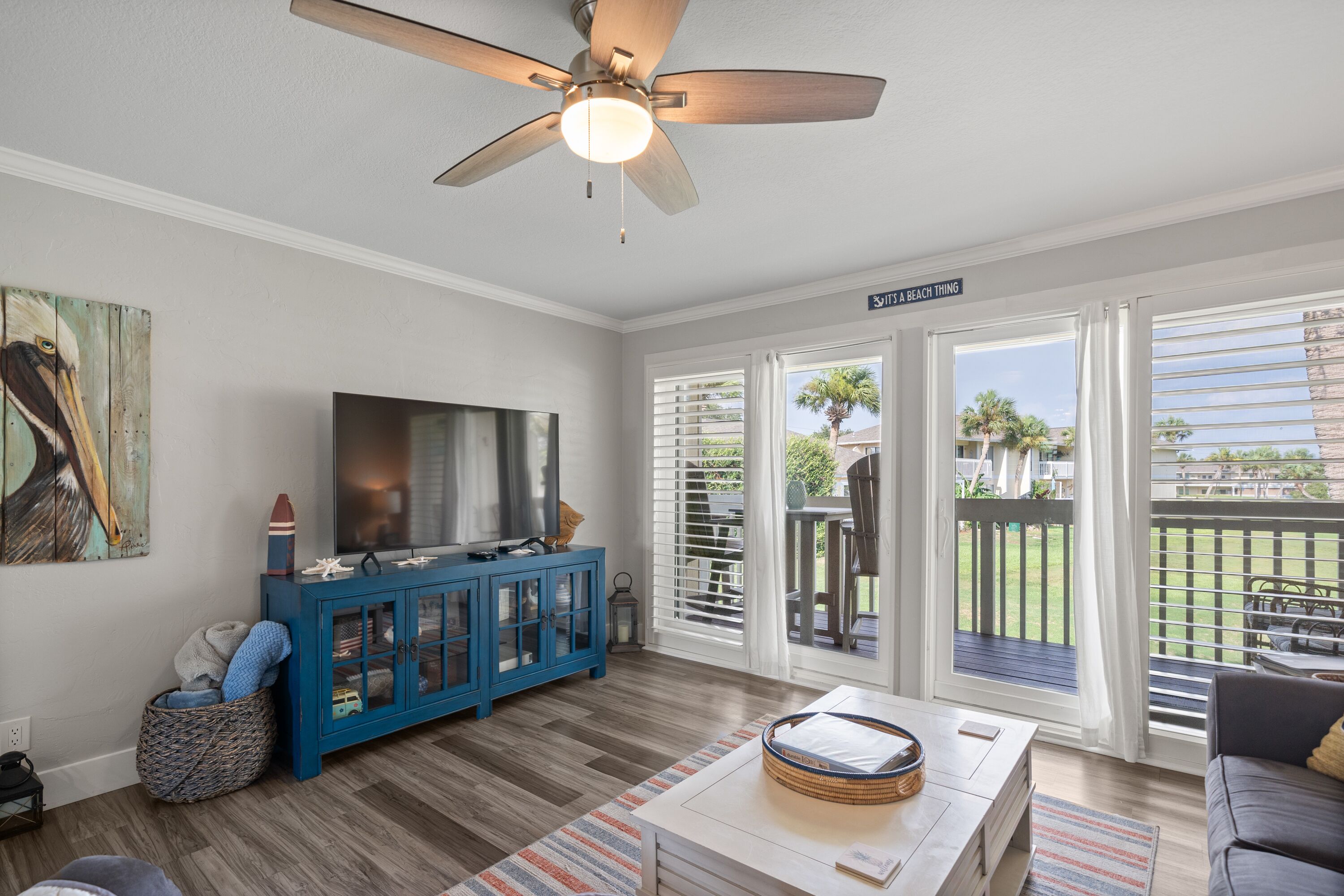 A living room with a TV, blue cabinet, wicker basket, and a ceiling fan.