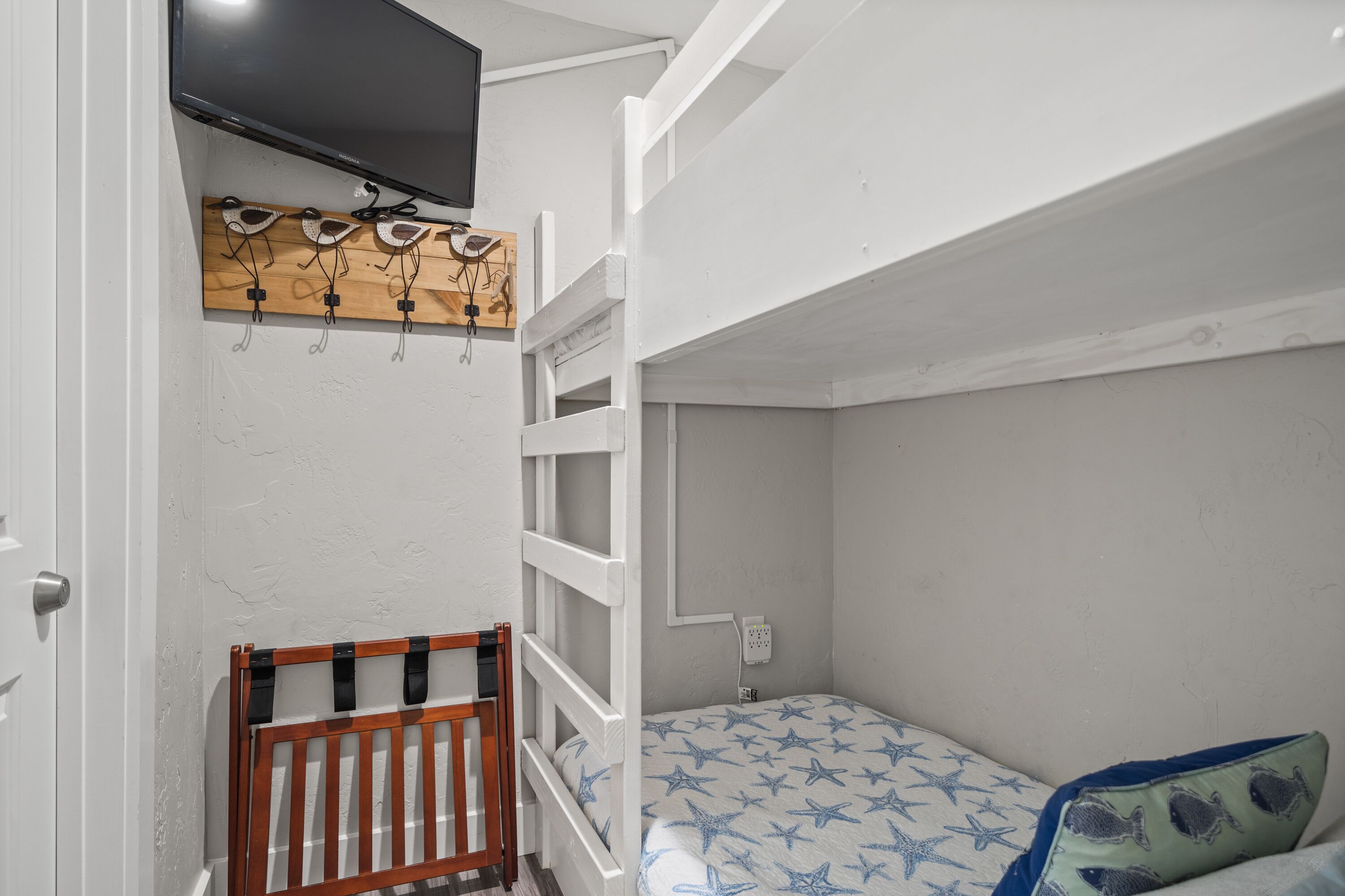A bedroom with a bunk bed, a wooden headboard, a bedside table, and a wall-mounted TV.