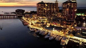 Un hotel frente al agua con varias edificaciones, un muelle con barcos y un espigón que se adentra en el agua.