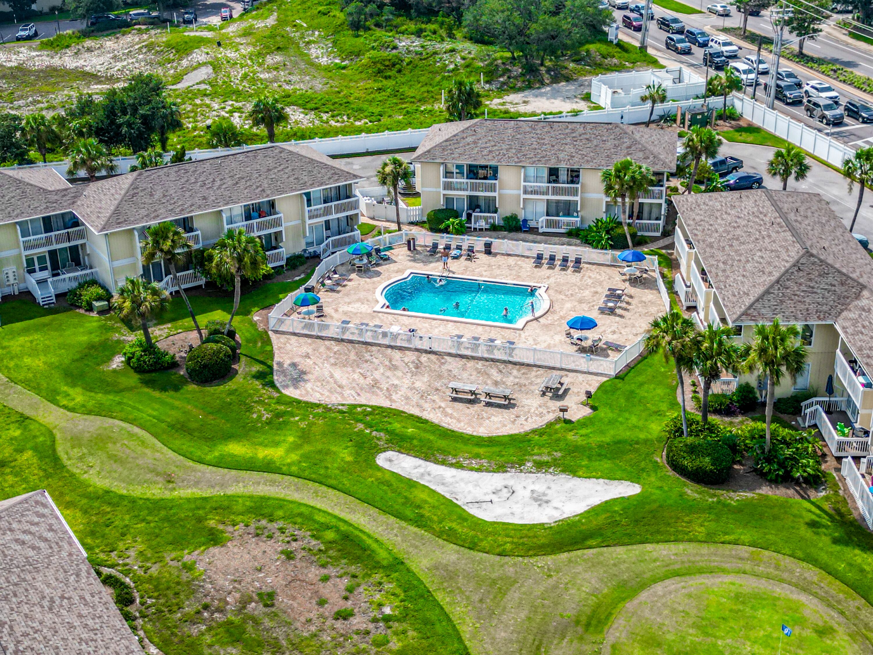 An aerial view of a resort with a central swimming pool, multiple guest rooms, and a well-maintained lawn.