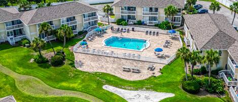 An aerial view of a resort with a central swimming pool, multiple guest rooms, and a well-maintained lawn.