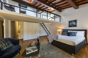 Een slaapkamer met een bed, een slaapbank, een bijzettafeltje, een ladder en een schilderij aan de muur.