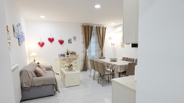 A modern living room with a sofa, a dining table with chairs, and decorative heart-shaped items on the wall. - Apartment in the heart of the Spanish Quarter, next to Via Toledo. (Napoli)