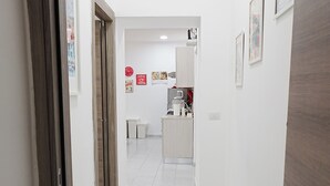 A hallway with white walls, a tiled floor, and a kitchen area in the distance. - Apartment in the heart of the Spanish Quarter, next to Via Toledo. (Napoli)