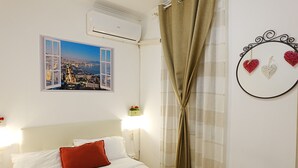 A hotel room with a bed, a window with a cityscape view, an air conditioner, a wall-mounted light, and a curtain. - Apartment in the heart of the Spanish Quarter, next to Via Toledo. (Napoli)