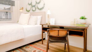 Een slaapkamer met een bed, een bureau, een stoel, een lamp, een plant en een decoratie aan de muur.