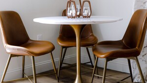 Een eetgedeelte met een ronde tafel, vier bruine leren stoelen en een gouden voet.