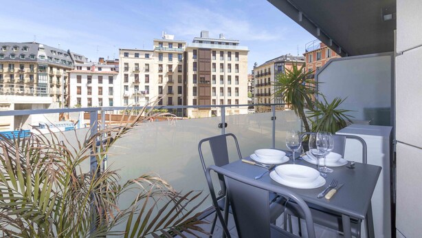 A balcony with a table set for dining, overlooking a cityscape with buildings. - Viena | The Rentals Collection (San Sebastián)