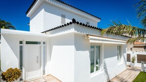 Una casa moderna de color blanco con techo de tejas, una terraza de madera y un pequeño jardín.
