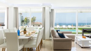 Una sala de estar moderna con comedor, ventanas amplias, vista a la piscina y un televisor de pantalla plana.