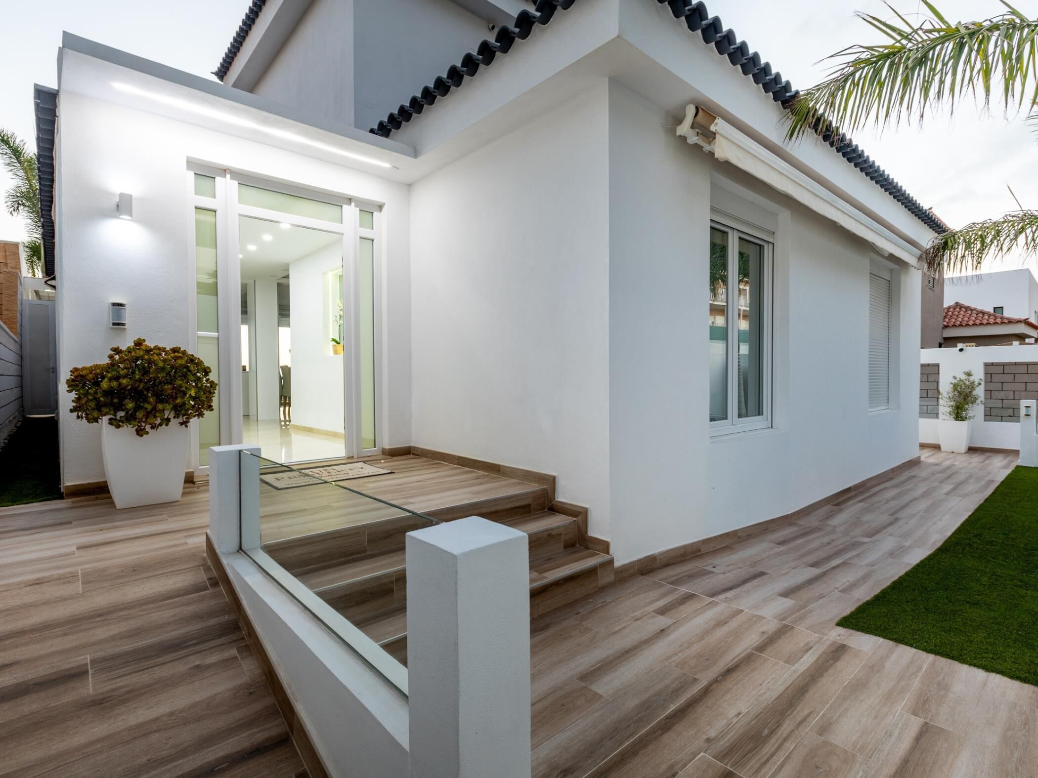 A modern house with a white exterior, a wooden staircase, and a small garden area.