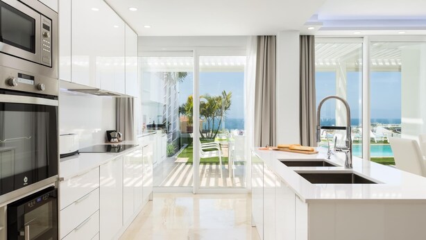 Una cocina moderna con electrodomésticos integrados, una isla grande con fregadero y vistas a una piscina y palmeras.