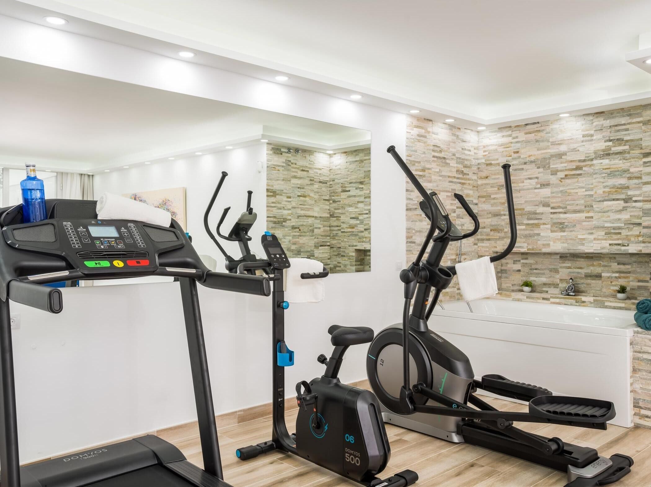 A home gym with a treadmill, elliptical, and stationary bike, a large mirror, and a stone-patterned wall.