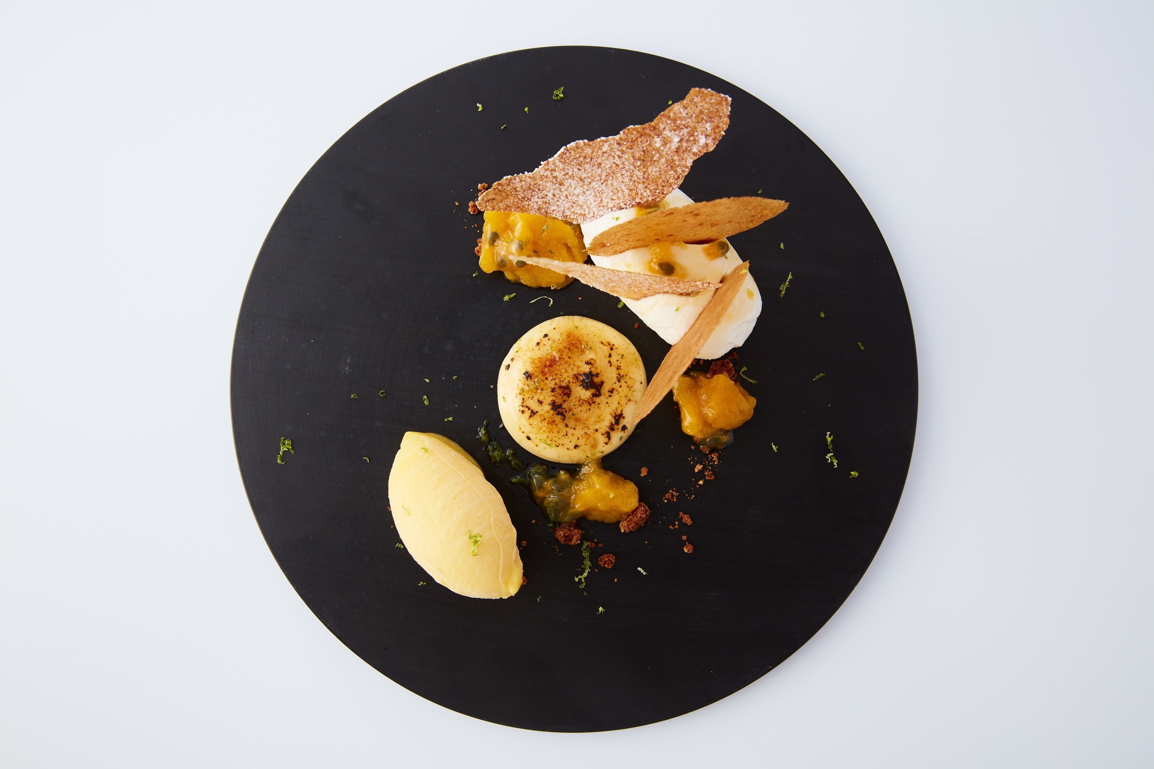 A black plate with a dessert consisting of a scoop of ice cream, a piece of cake, and a caramelized fruit topping.