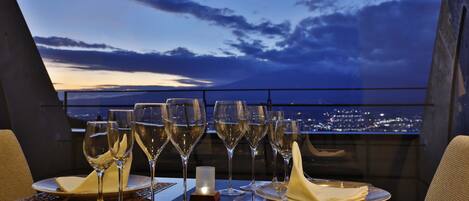 A table set for a meal with wine glasses, a candle, and a view of a cityscape at dusk.