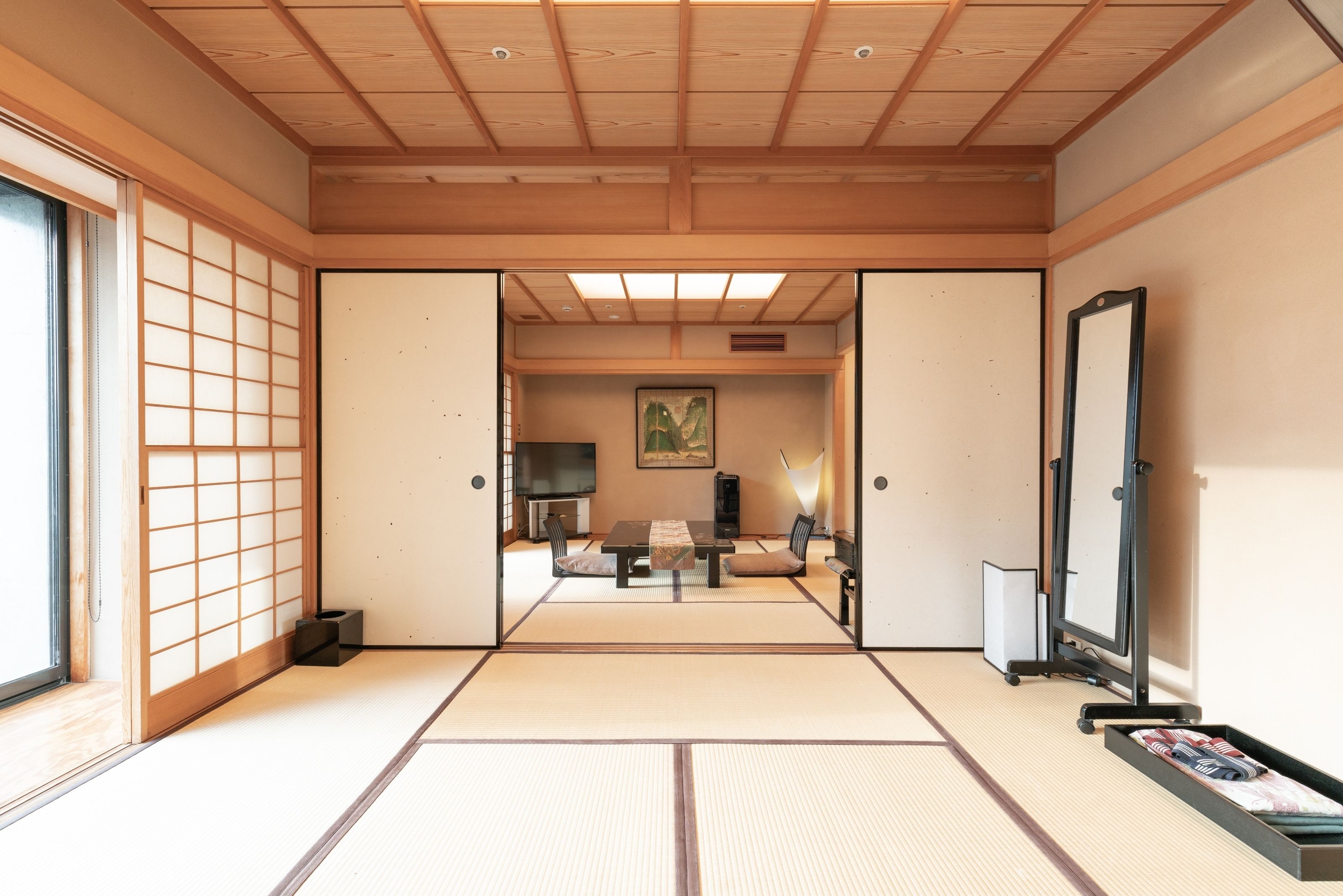A traditional Japanese room with tatami flooring, a sliding door, a television, a painting, and a mirror.
