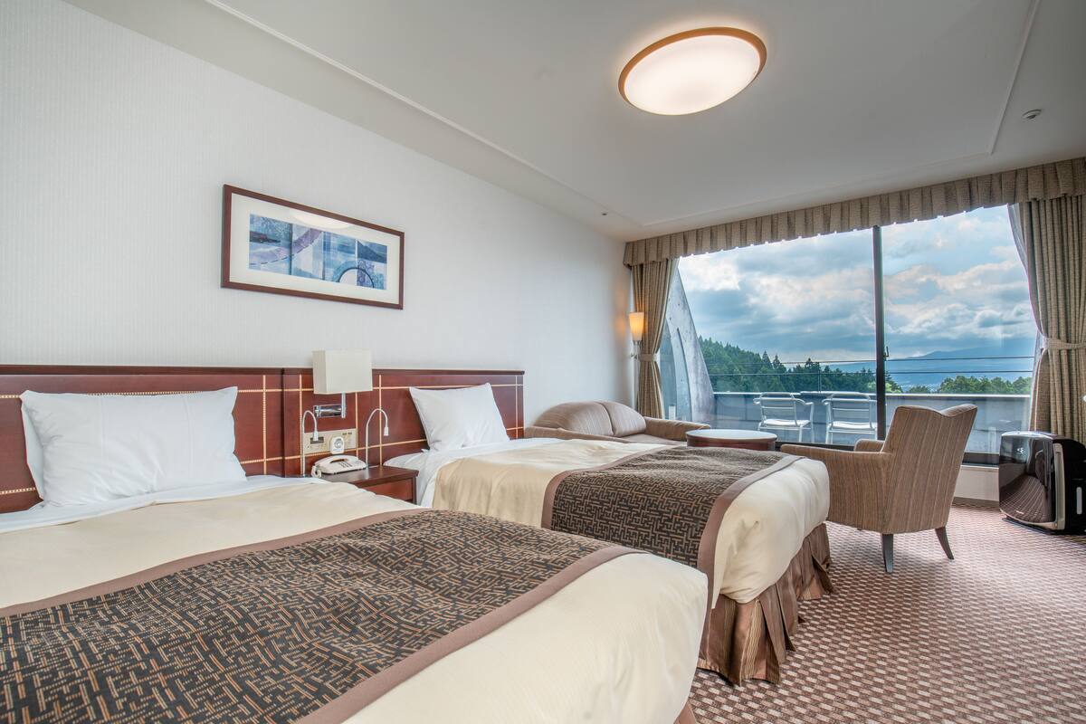 A hotel room with two beds, a large window with a view, a chair, and a television.