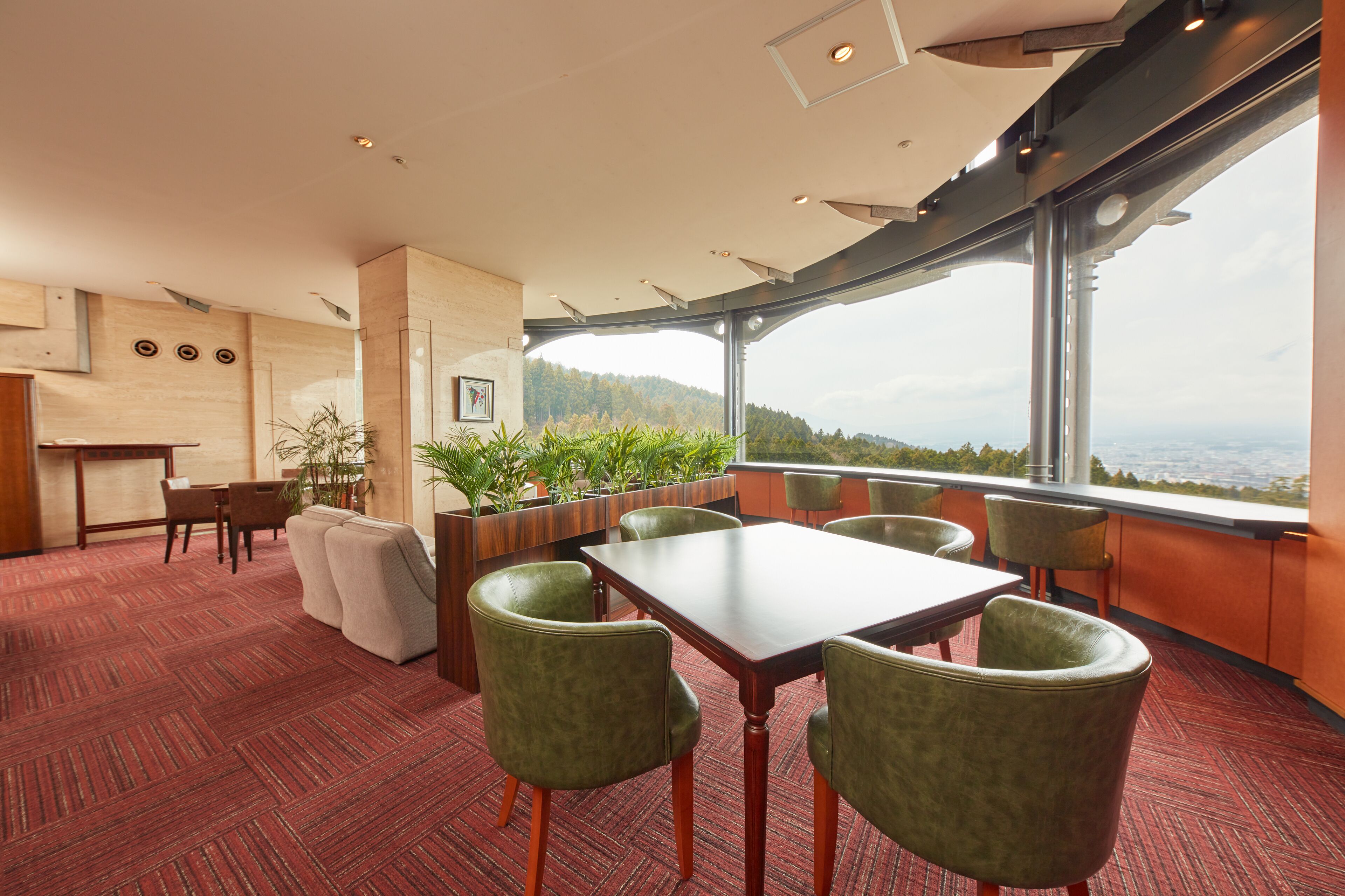 A modern conference room with a large table and green chairs, a wooden reception desk, and a view of a forested landscape through large windows.